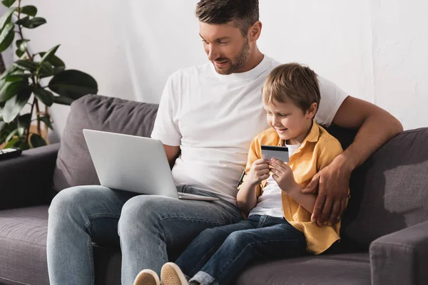 Homem Bonito Usando Laptop Enquanto Seu Filho Sorridente Segurando Cartão — Fotografia de Stock