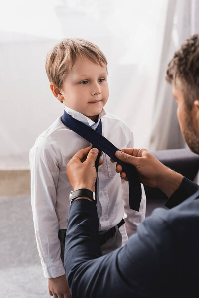 selective focus of businessman putting tie on cute, serious son at home