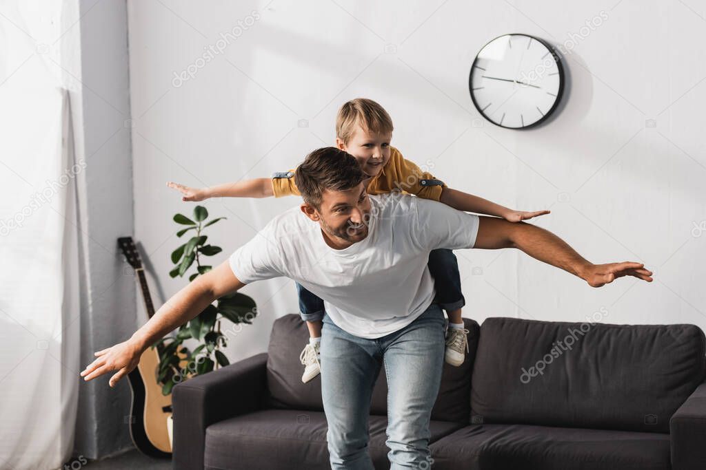 cheerful father piggybacking happy son imitating flying with outstretched hands