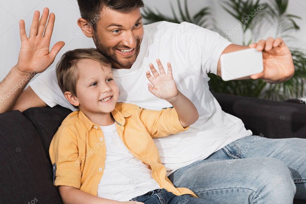 happy father and son waving hands dring video chat on smartphone