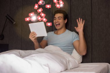 Yakışıklı melez adam, dijital tablette sanal kalplerin yanında görüntülü sohbet ederken el sallıyor. 