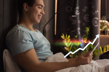 Gülümseyen karışık ırk adamı sanal dolar yakınlarındaki yatakta dijital tablet kullanıyor ve artan oranıyla grafiğe yakın avro tabelaları 