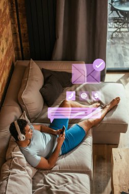 Melez ırk adamının dinlenme, müzik dinleme ve sanal konuşma baloncuğu yanında akıllı telefon ve yeni mesaj illüstrasyonlu zarf kullanımının genel görünümü 