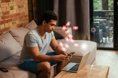 Laptop ve kalplerin yanında akıllı telefon kullanan yakışıklı, karışık ırk serbest çalışanı. 