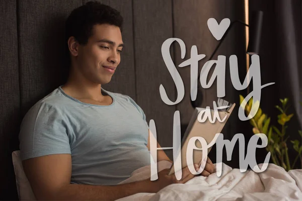 Smiling Mixed Race Man Reading Book Stay Home Lettering Bedroom — Stock Photo, Image