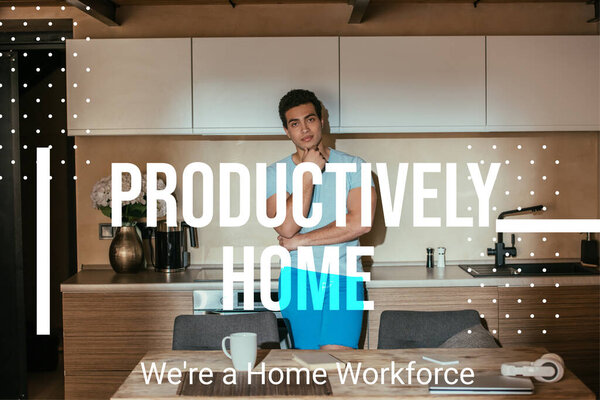pensive mixed race man standing near coffee cup, book, headphones, laptop and productively home, were a home workforce lettering 