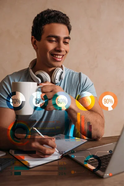 Happy Mixed Race Man Holding Coffee Cup While Writing Laptop — Stock Photo, Image