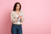 Krásná brunetka žena pomocí smartphone na růžovém pozadí, koncept těla pozitivní 