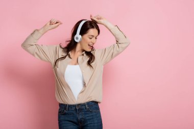 Beautiful woman in headphones dancing and singing on pink background clipart