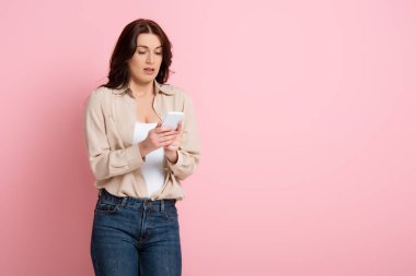 Güzel esmer kadın pembe arka planda akıllı telefon kullanıyor, vücut pozitifliği kavramı. 