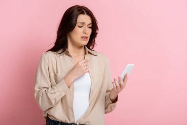 Pembe arka planda akıllı telefonu tutan endişeli kadın, vücut pozitifliği kavramı 