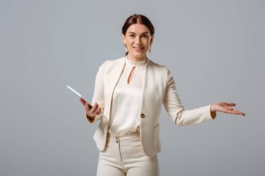 Çekici iş kadını kameraya gülümsüyor ve gri tableti tutarken eliyle işaret ediyor. 