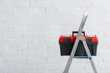 Alet çantası beyaz duvarın yanındaki metal merdivende.