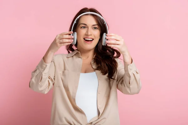 Mujer Positiva Sosteniendo Auriculares Inalámbricos Sobre Fondo Rosa — Foto de Stock