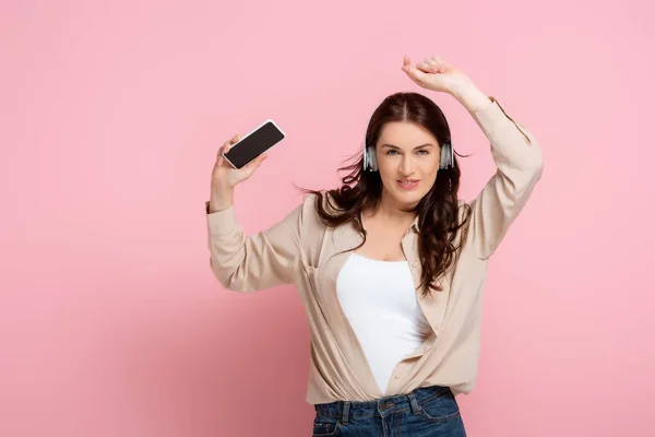 Mulher Positiva Fones Ouvido Segurando Smartphone Olhando Para Câmera Fundo — Fotografia de Stock