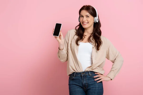 Gyönyörű Fülhallgató Gazdaság Smartphone Mosolygós Kamera Rózsaszín Háttér — Stock Fotó