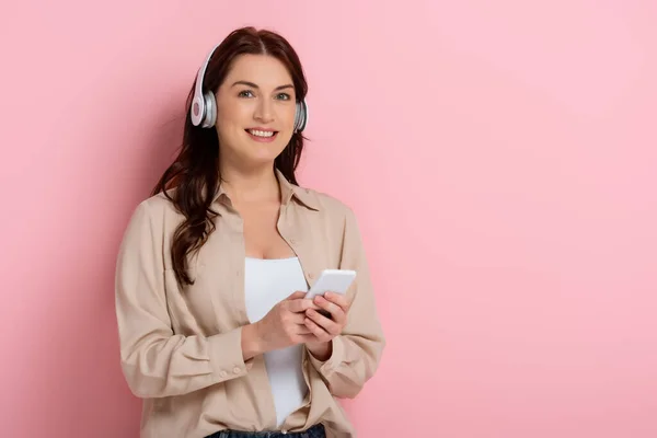 Attractive Woman Smiling Camera While Using Headphones Smartphone Pink Background — Stock Photo, Image
