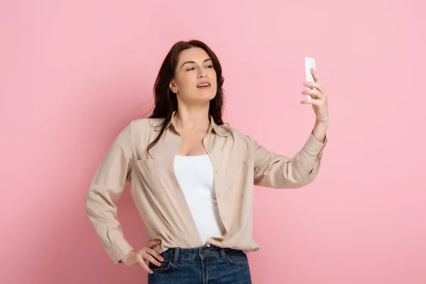 美しい女性はピンクの背景にスマートフォンで自撮り 体の肯定的な概念 — ストック写真