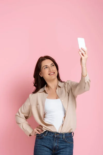 迷人的女人带着粉红背景的智能手机 一边笑一边自拍 — 图库照片