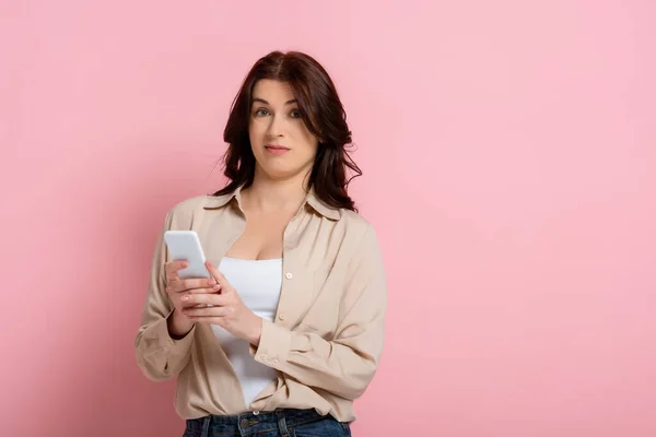 Donna Confusa Utilizzando Smartphone Guardando Fotocamera Sfondo Rosa — Foto Stock