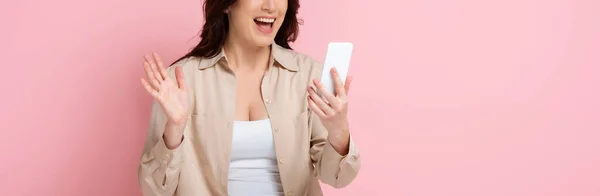 パノラマショットの正の女性持っていますビデオ通話上のスマートフォン上のピンクの背景 — ストック写真