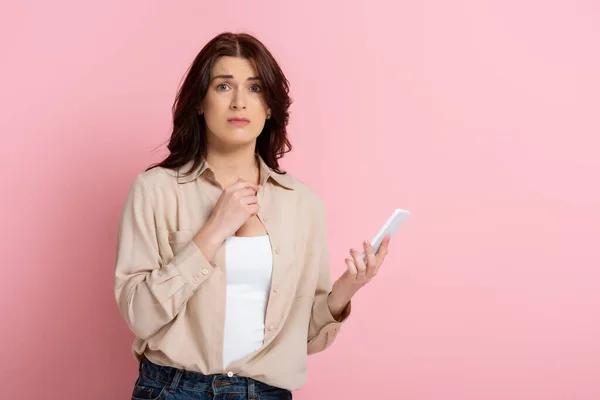 Endişeli Kadın Pembe Arka Planda Akıllı Telefonu Tutarken Kameraya Bakıyor — Stok fotoğraf