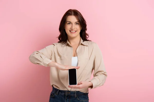 ピンクの背景に空白の画面でスマートフォンを保持する美しい笑顔の女性 — ストック写真