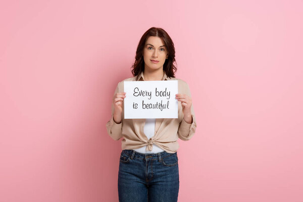 Beautiful woman holding card with every body is beautiful lettering on pink background
