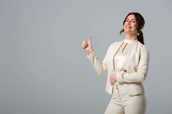 Beautiful smiling businesswoman showing thumb up isolated on grey 