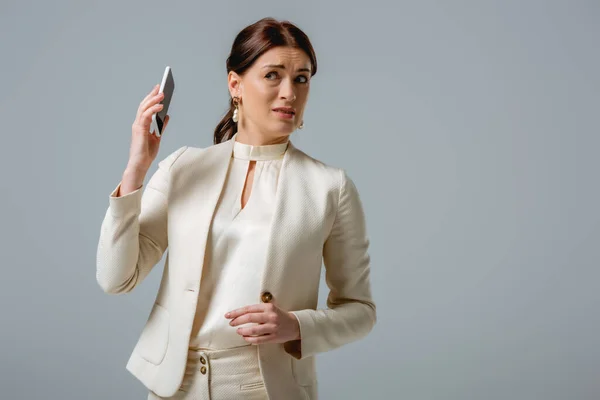 灰色で隔離された正式な摩耗保持スマートフォンで混乱した女性 — ストック写真