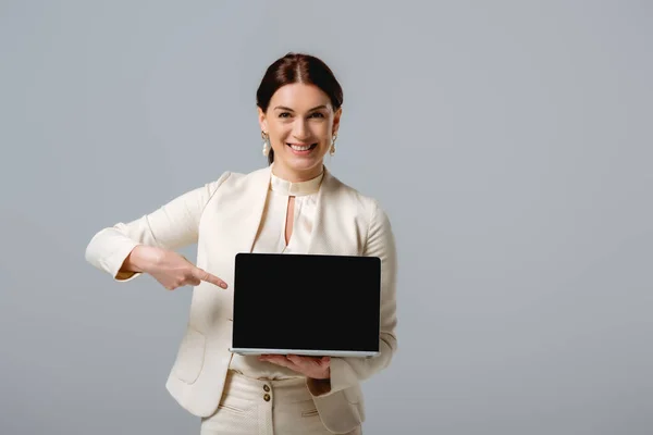 Piękna Bizneswoman Wskazująca Palcem Laptopa Uśmiechnięta Kamery Odizolowana Szaro — Zdjęcie stockowe