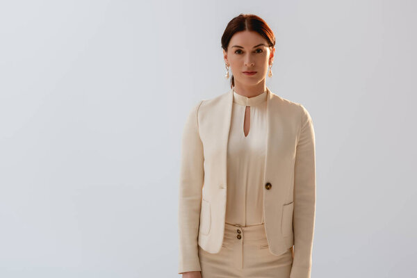 Beautiful brunette woman in formal wear looking at camera isolated on grey 