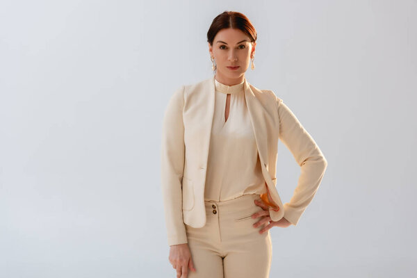 Attractive woman in formal wear with hand on hip looking at camera isolated on grey 