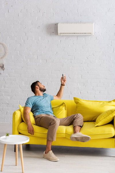 Young man switching air conditioner with remote controller in living room