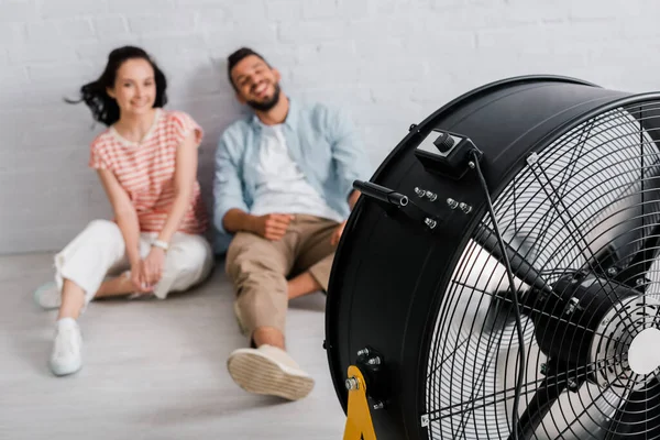 Foco Seletivo Ventilador Elétrico Perto Casal Sorridente Sentado Chão Casa — Fotografia de Stock