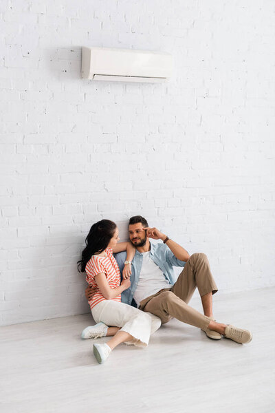 Handsome man hugging girlfriend while sitting together on floor under air conditioner 