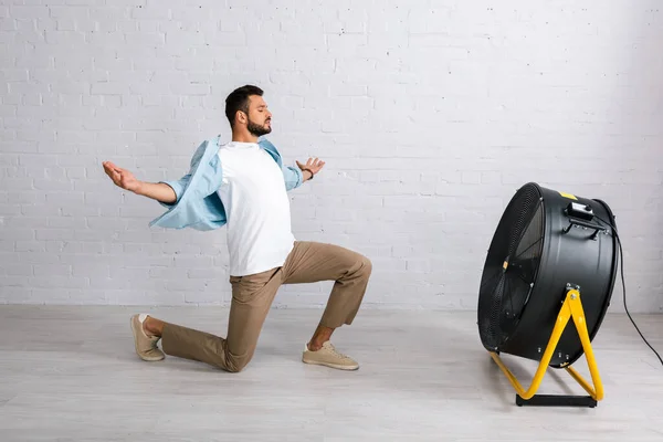 Schöner Mann Steht Auf Knien Neben Elektroventilator Auf Dem Boden — Stockfoto