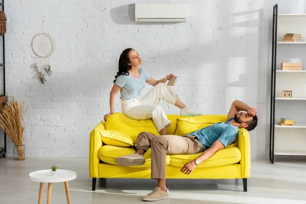 Woman Holding Book While Suffering Heat Boyfriend Couch Living Room — Stock Photo, Image