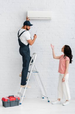 Klimayı tamir eden işçiye yakın eli olan bir kadının yan görüntüsü 