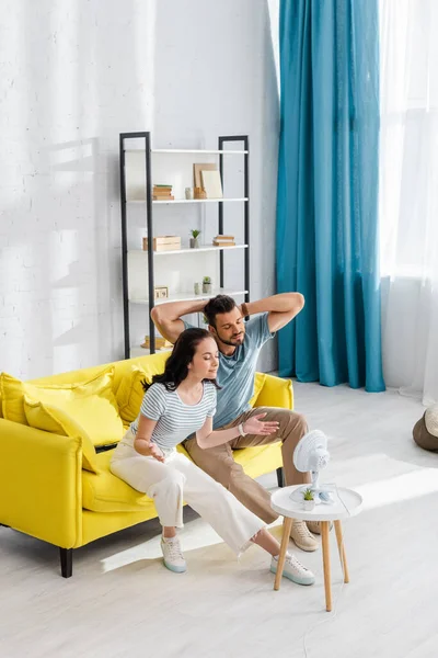 Jeune Couple Assis Sur Canapé Près Ventilateur Électrique Sur Table — Photo