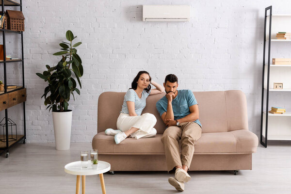 Selective focus of young couple looking at camera while sitting on couch in living room