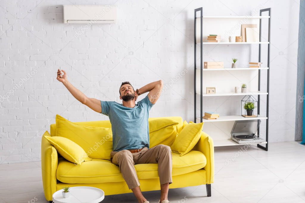 Handsome man switching air conditioner with remote controller in living room
