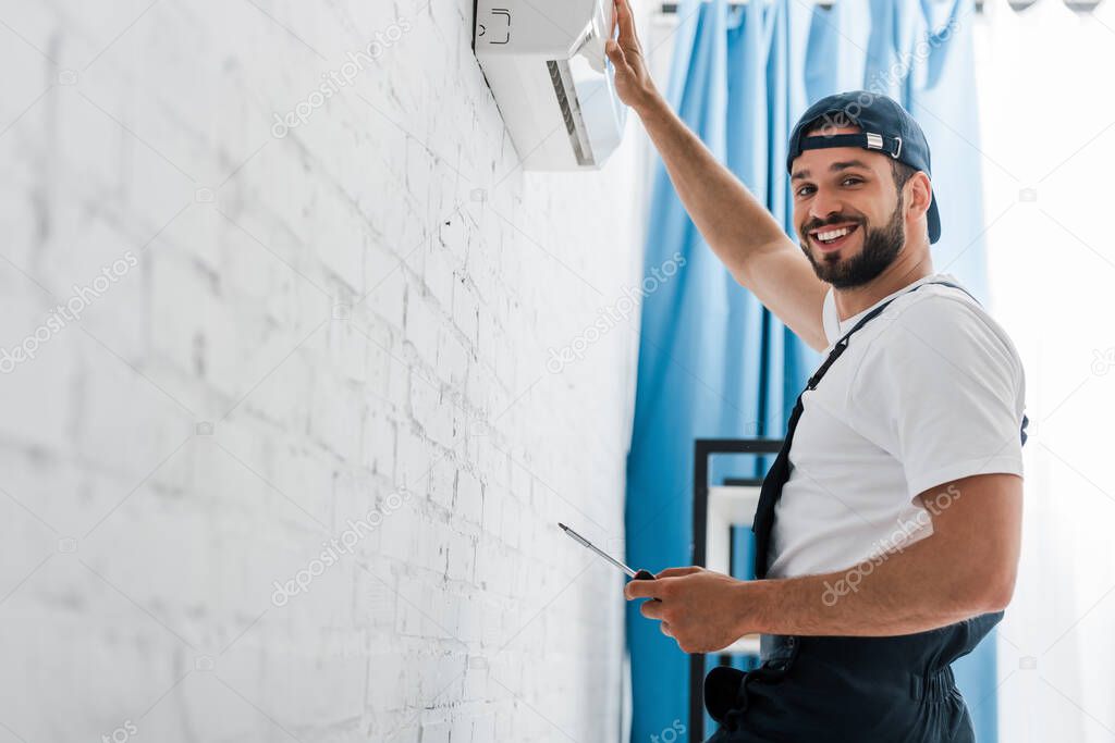 Smiling workman looking at camera while repairing air conditioner