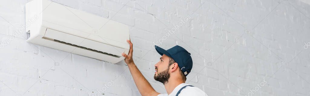 Panoramic crop of workman looking at air conditioner on wall