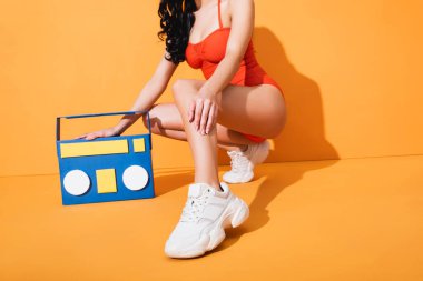 Spor ayakkabılı, mayo giymiş, kağıt kesikli müzik kutusunun yanında oturan şık bir kadın.
