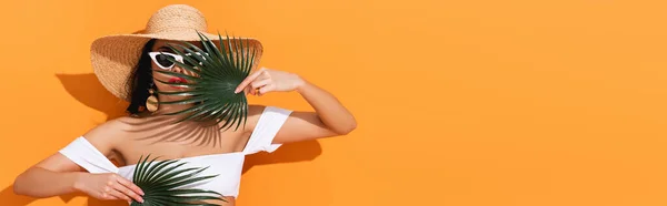 オレンジ色のヤシの葉を持つ水着 サングラス 麦藁帽子のファッショナブルな女性のパノラマショット — ストック写真