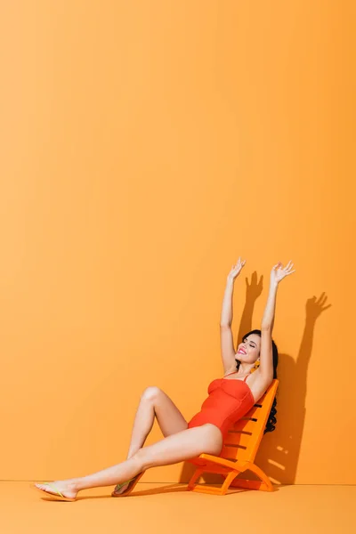 快乐的女孩 双手高举 坐在橙色的甲板椅子上 — 图库照片