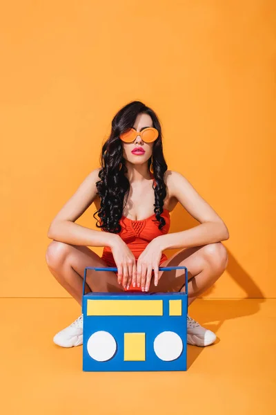 穿着运动鞋 泳衣和太阳镜的时髦女孩坐在橙色纸盒旁边 — 图库照片