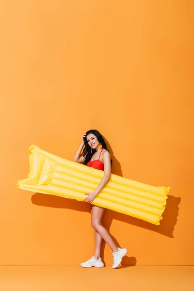 Happy Woman Swimsuit Sneakers Holding Inflatable Mattress Touching Hair Orange — Stock Photo, Image