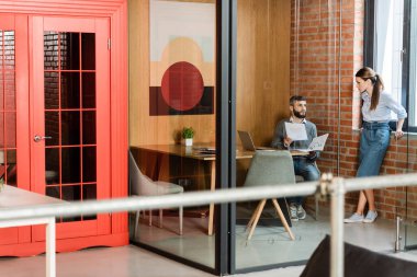 Çekici iş kadınının seçici odak noktası, ofiste belgeleri tutan sakallı iş arkadaşına bakıyor.
